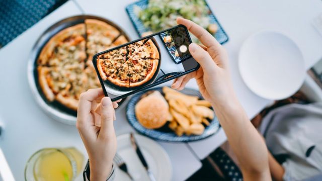 Pessoa fotografando pizza com celular