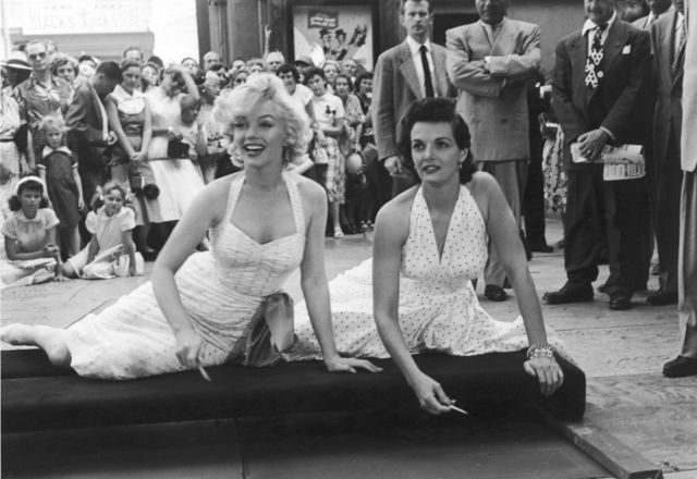 Las actrices estadounidenses Marilyn Monroe (1926 - 1962) (izquierda) y Jane Russell se sientan en un cojín y se preparan para firmar sus huellas de pies y manos en el cemento frente al Grauman's Chinese Theatre mientras promocionan su película, 'Los caballeros las prefieren rubias', Hollywood , California, 26 de junio de 1953.