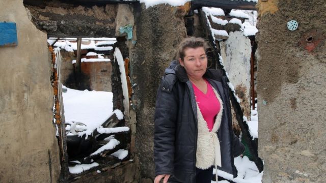 سيدة تقف خارج منزلها الذي دمرته قذيفة بالقرب من دونيتسك