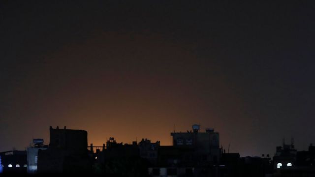 Luz brillando detrás de los edificios de un barrio después de las huelgas en Sana'a, Yemen, el sábado