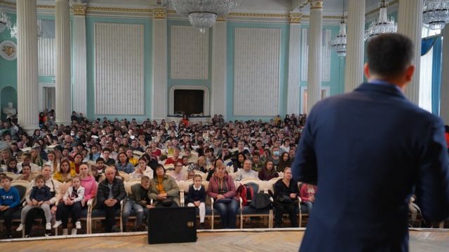 Pastor fala em palco a centenas de fiéis sentados