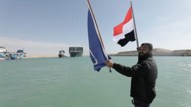 رجل يلوح بالعلم المصري لدى مشاهدته سفينة إيفر غيفن تبحر في قناة السويس بعد تعويمها.