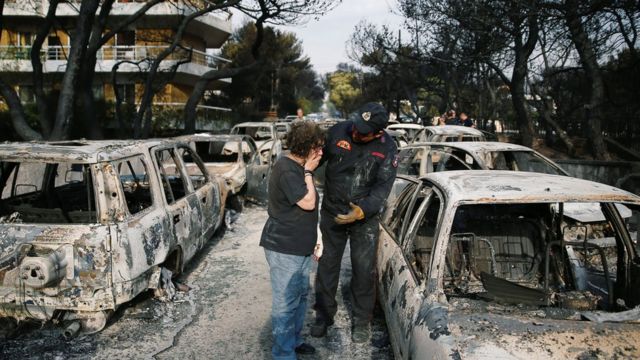 Mulher e integrante da equipe de resgate fazem buscas em meio a carros queimados por incêndio na Grécia, próximo à Atenas, em 24 de julho de 2018