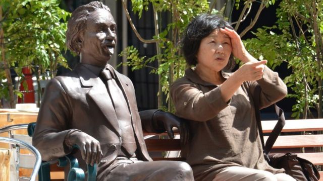 Una señora sentada en un banco con una estatua de Einstein