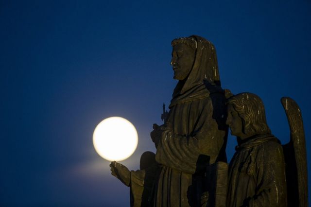 The pink supermoon rises behind statues on Charles Bridge in Prague, Czech Republic