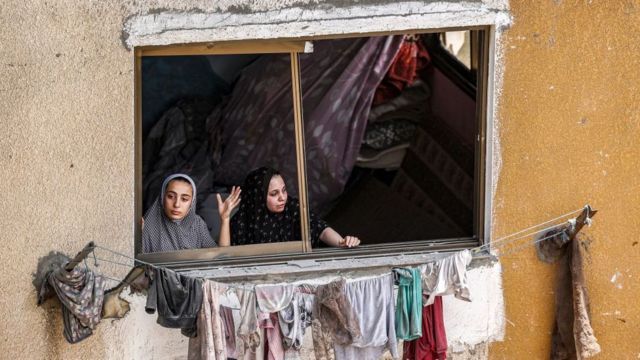 Wanita melihat melalui jendela yang pecah di Jalur Gaza setelah serangan Israel.