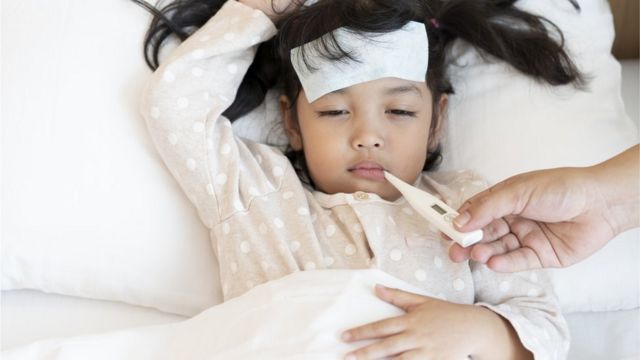 Criança na cama com febre e com termômetro na boca