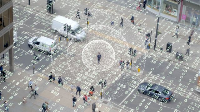 Fotografia colorida mostra pessoas na rua e números de programação flutuando no ar