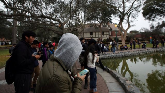Jóvenes mirando sus celulares en un parque frente a una laguna