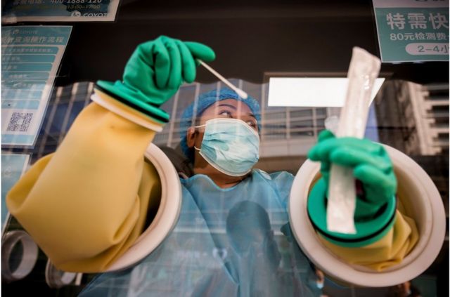 A medical worker performs a nucleic acid test at a booth on the streets of Beijing.