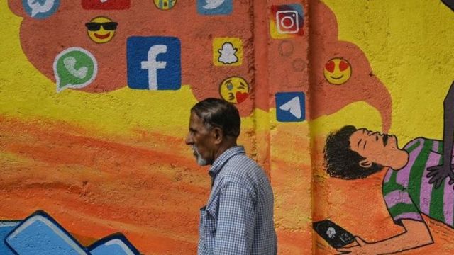 رجل يسير أمام جدارية في الهند تظهر شخصاً يتقيأ تطبيقات التواصل الاجتماعي