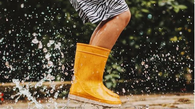 Garçon en bottes de caoutchouc sautant sous la pluie.