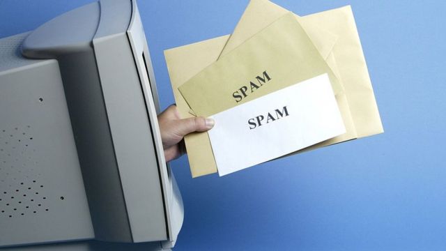 Mano sale de la pantalla de una vieja computadora con un puñado de cartas en la mano que dicen "Spam".