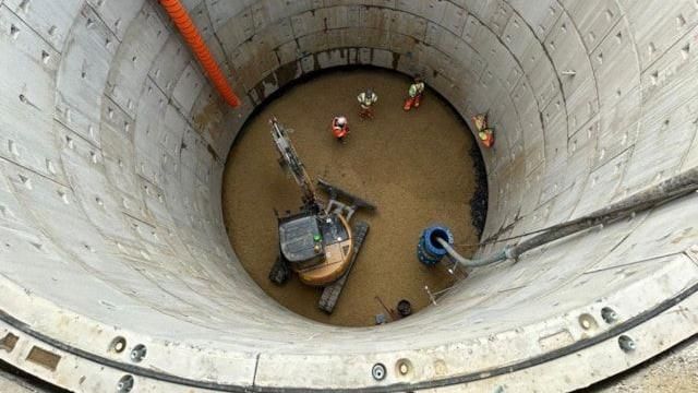 An aerial shot of a digger and three workmen at the bottom of a large hole