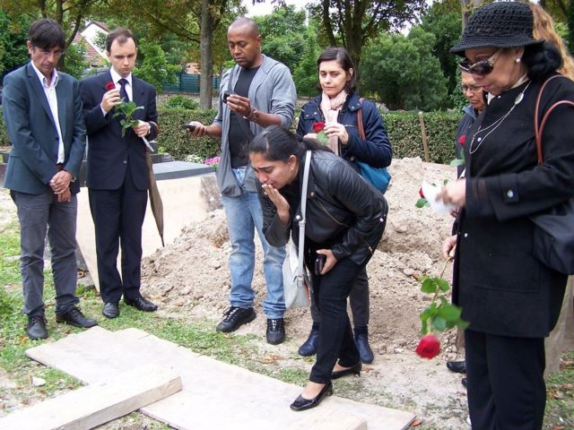 Pessoas chorando e com rosas perto de túmulo