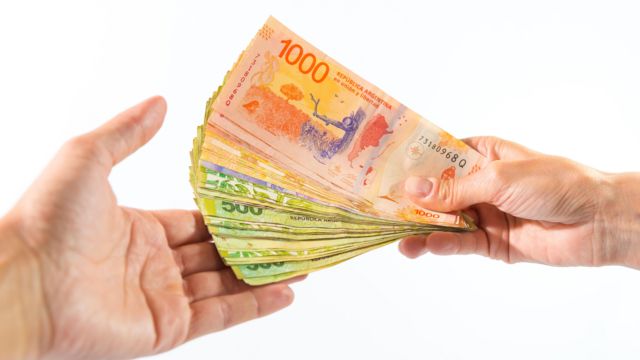 Una mano entregando a otra billetes de 1000 y 500 pesos argentinos