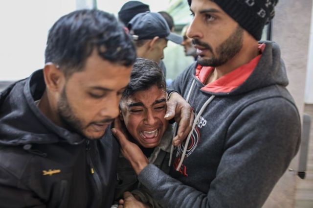 Um jovem palestino chora abraçado por outras duas pessoas em um necrotério de Gaza