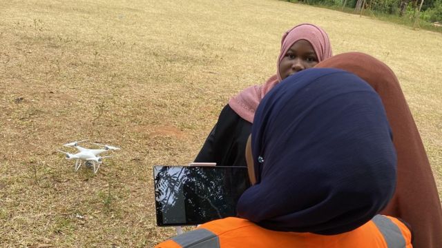 Trois femmes de Zanzibar portant un foulard tiennent un smartphone avec un drone au sol derrière elles.
