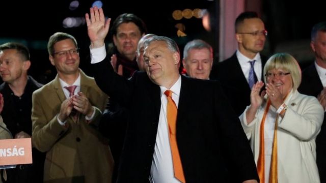 Orban (centro), um homem branco de meia idade e terno, acena para a plateia cercado do aliados