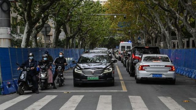 People ride scooters next to barricades on Wulumuqi street, named for Urumqi in Mandarin, in Shanghai on November 28, 2022, a day after protests against China's Covid-19 restrictions following a deadly fire in Urumqi, the capital of the Xinjiang region.