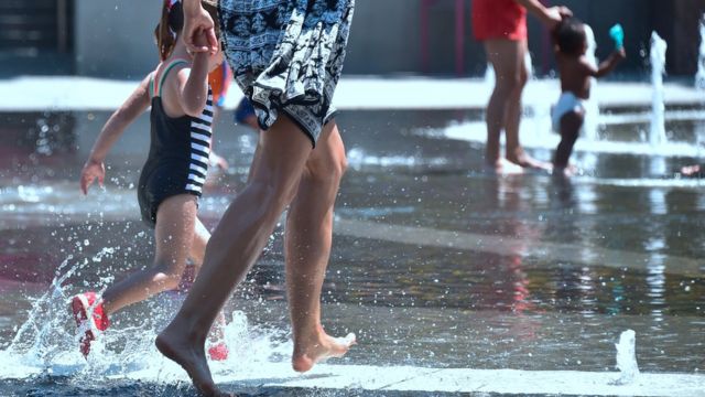 امرأة وطفلها يسيران في مياه نافورة في يوم حار