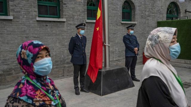 Hui Muslim women wear masks as they wait for officers to raise China's national flag before Eid al-Fitr prayers at the historic Niujie Mosque on May 13, 2021 in Beijing, China