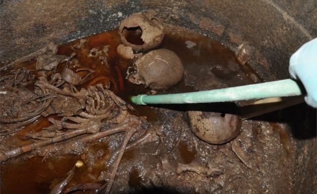 Three skeletons from the sarcophagus pictured submerged in red-coloured sewage water