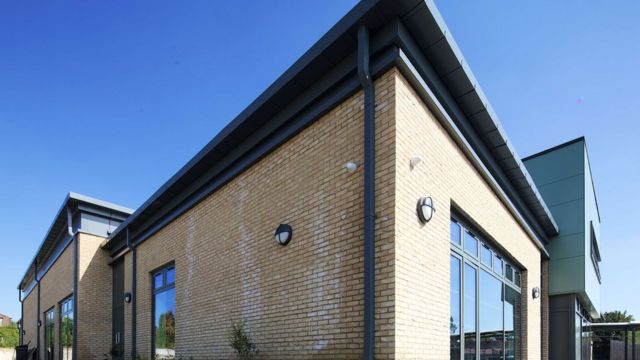 A new school building, built in brick with large windows and modern grey blocks jutting out of the side for extra rooms.