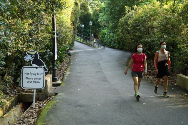 People wearing face masks against Covid walk past a sign encouraging the use of masks at Singapore's Botanic Gardens