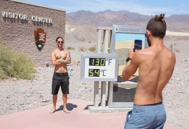 Dua pria berdiri di samping layar digital yang mencatat suhu 54C di Furnace Creek selama gelombang panas di Taman Nasional Death Valley di Death Valley, California, 16 Juli 2023.