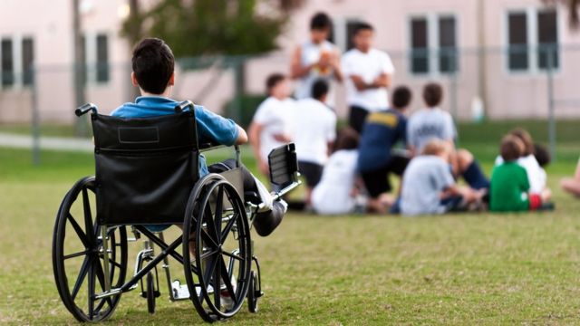 Un niño en silla de ruedas alejado de un grupo de jóvenes.