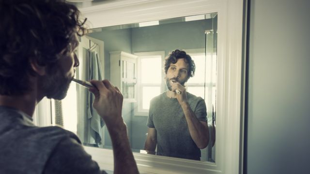 El hombre se cepilla los dientes frente al espejo.