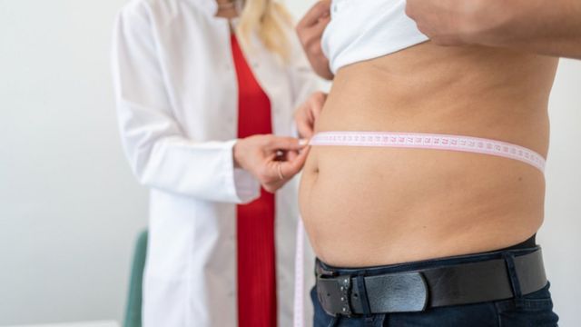 Una profiesonal de la salud mide la barriga de un hombre.