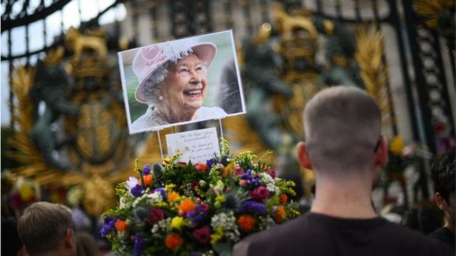 Une photo de la défunte reine Elizabeth II parmi les hommages floraux devant les portes du palais de Buckingham à Londres.