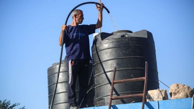 رجل يملأ خزانا بالمياه فوق منزله في غزة