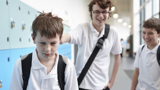 Boy holding classmate's head in locker room at school