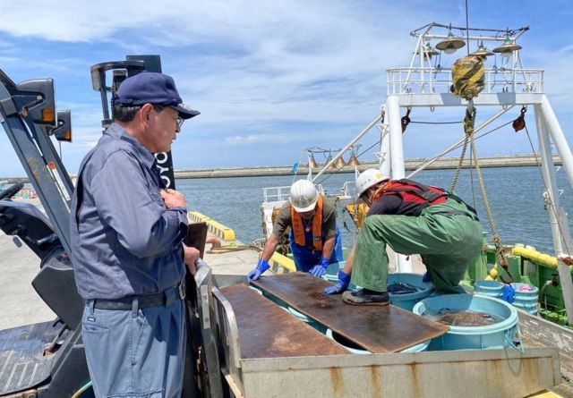 Toru Takáhashi y trabajadores en un barco de pesca amarrado a un embarcadero de cemento.