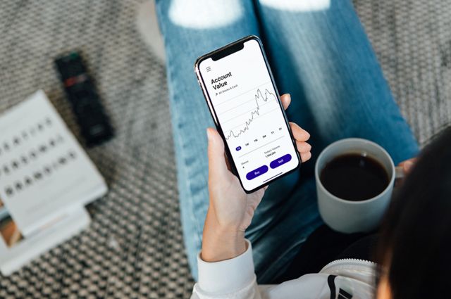 A woman looking at an investment app while drinking coffee