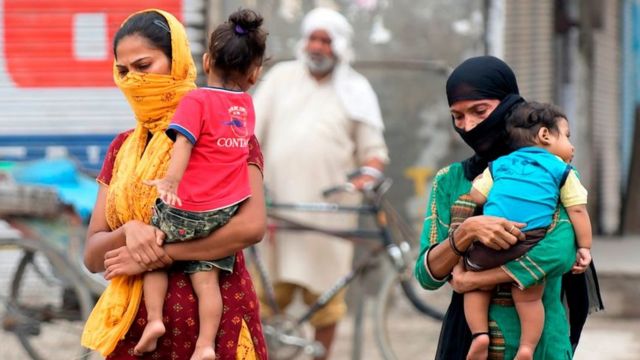 Women wearing masks carry and their children and walk on the outskirts of Amritsar on September 5, 2020.