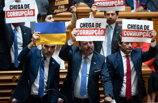 Deputados do Chega seguram cartazes com bandeira da Ucrânia e com frase "chega de corrupção" durante discurso de Lula no Parlamento português