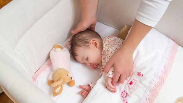 Manos de una mujer colocan a un bebé en su cuna
