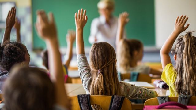 Crianças na sala de aula com as mãos erguidas