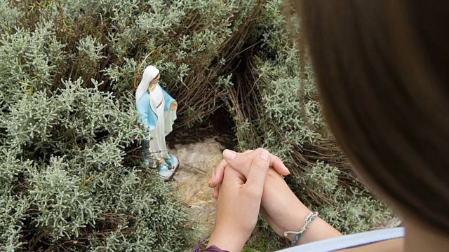 Mujer rezando ante una estatuilla de la Virgen María en el campo