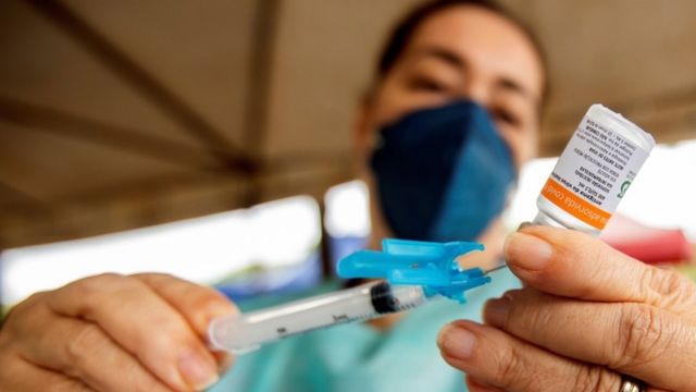 Profissional de máscara e jaleco insere seringa em vidro de vacina