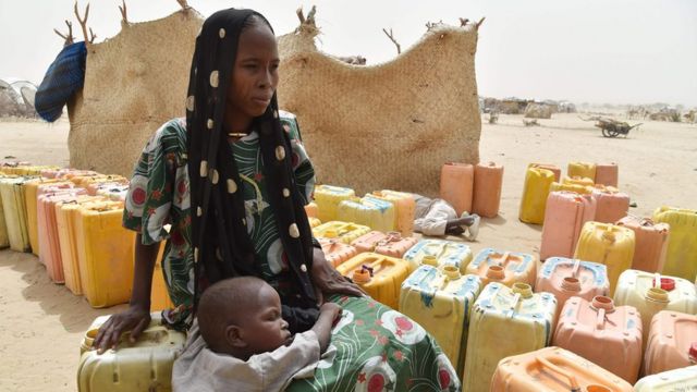 A displaced woman sits on a water can as she waits with her child to during a water distribute by agents from the UN System in a refugees camp of Kidjendi, around Diffa, southeastern Niger, on June 19, 2016.