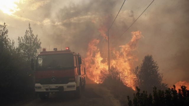 Chamas e fumaça são vistas nas proximidades de árvores e de um carro do corpo de bombeiros durante incêndio florestal na Grécia em 23 de julho de 2018