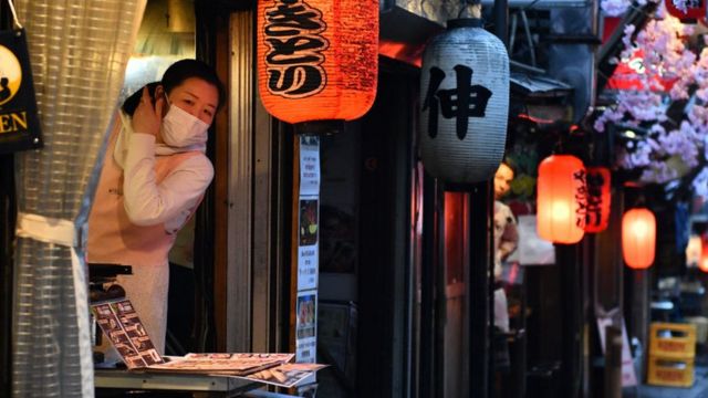 A woman wearing a face mask looks out from a yakitori restaurant in a traditional dining area on March 19, 2020 in Tokyo, Japan.