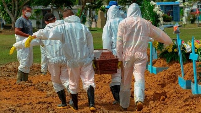 Trabalhadores carregam um caixão num cemitério