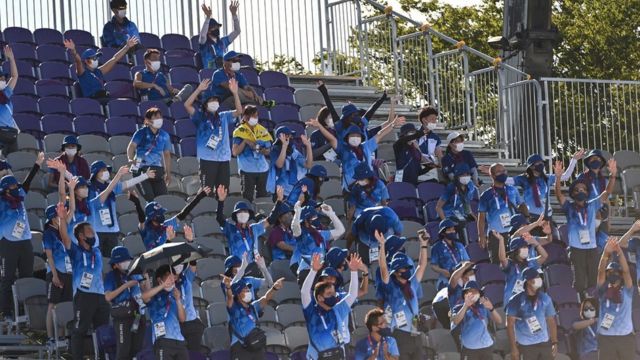 Dozens of volunteers at an Olympic event clapping.