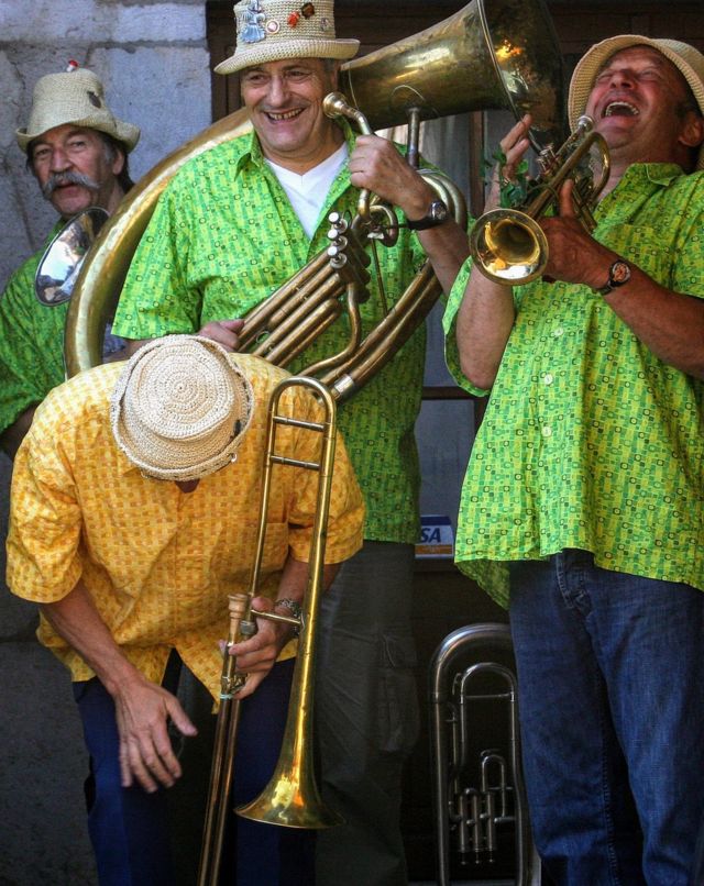 Los músicos de una banda de vientos, con sus instrumentos y camisas coloridas, estallan en carcajada